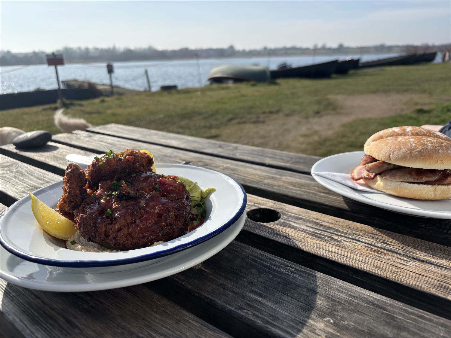 A photo of two meals on a picnic table outside the Mere cafe with Hornsea Mere in the back ground